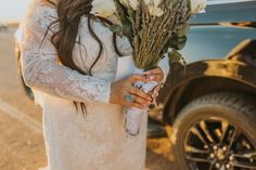 a woman in a wedding dress holding flowers next to a truck with it's door open