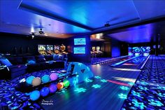 a bowling alley is lit up with blue lights and colorful balls on the floor in front of it