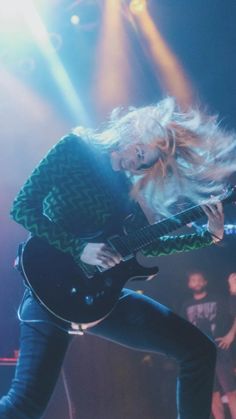 a woman with blonde hair playing an electric guitar in front of other people on stage