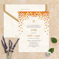 an orange and yellow wedding card on top of a marble surface with flowers in the foreground