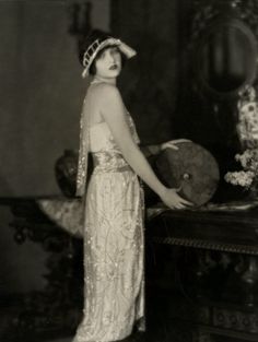 an old black and white photo of a woman in a long dress with a hat on her head