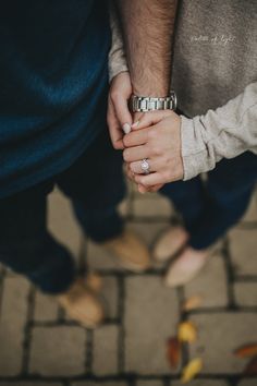 two people holding hands while standing next to each other on a brick floor with their wedding rings