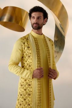 Summer Love Shrug Set | Jatin Malik Introducing our vibrant lemon yellow shrug set, adorned with intricate floral hand embroidery and three types of embroidered lapels in shades of yellow. This ensemble radiates freshness and sophistication, capturing attention with its intricate detailing and vibrant color palette. Paired with an embroidered shoulder-button kurta and tapered trousers, this outfit offers a perfect balance of elegance and contemporary style. Ideal for special occasions, this ensemble is sure to make a statement with its unique design and impeccable craftsmanship. Included in purchase: Shrug Set, Kurta, Trousers Product Specification Color: Yellow Fabric: Linen Silk Occasion: Engagement, Wedding, Bridal, Reception Style: Shrug Set, Kurta, Trousers Care: Dry Clean Work: Hand Yellow Kurta With Resham Embroidery For Reception, Yellow Kurta For Diwali Reception, Yellow Kurta With Dupatta For Reception, Festive Yellow Kurta For Reception, Yellow Long Sleeve Sets For Reception, Yellow Long Sleeve Reception Set, Yellow Traditional Wear With Chikankari Embroidery For Reception, Yellow Kurta For Eid Reception, Elegant Yellow Designer Wear Sets