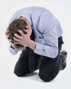 a man with his head in his hands is sitting on the ground and looking down