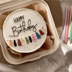 a birthday cake with the words happy birthday written on it in black writing and colorful tassels