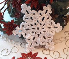 a crocheted snowflake sitting on top of a table next to red flowers