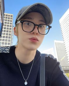 a woman wearing glasses and a hat is posing for the camera with buildings in the background