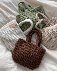 four crocheted purses sitting on top of a white bed next to each other