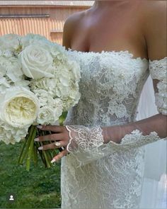 a woman in a wedding dress holding a bouquet of white roses and greenery,