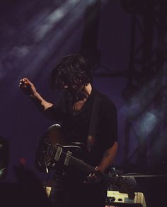 a man holding a guitar while standing on top of a stage