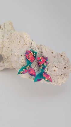 a pair of pink and blue earrings sitting on top of a white piece of rock