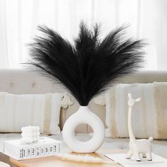 a black feather is in a white vase on a table next to a book and toy giraffe