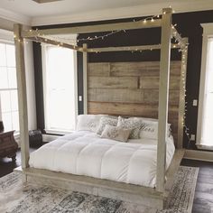 a white bed sitting in the middle of a bedroom next to two windows with lights on them