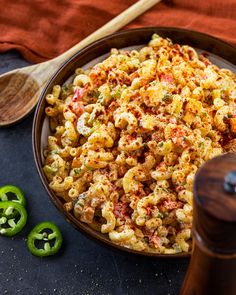 a bowl filled with macaroni salad next to green peppers and a wooden spoon