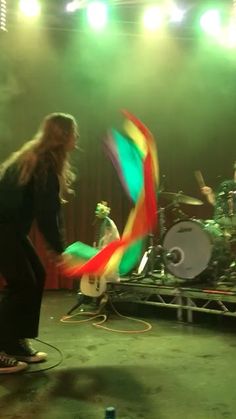 a man with long hair standing in front of a drum set on top of a stage