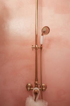 a pink bathroom with gold faucet and shower head