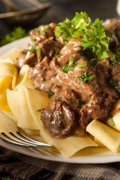 a white plate topped with pasta and meat covered in sauce on top of a table