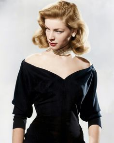 a woman with blonde hair wearing a black dress and pearls on her neck, posing for the camera