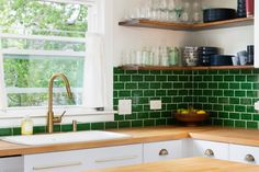 a kitchen with green tiles and wooden counter tops in front of a window, next to a sink