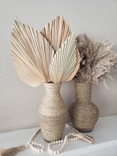 two vases sitting on top of a white shelf next to some plants and beads