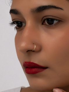 a woman wearing a nose ring with a gold nose pin in her right hand and red lipstick on the other side