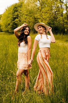 two women standing in tall grass with hats on their heads and one holding the other's hand