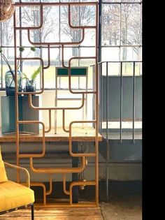 a yellow chair sitting in front of a window next to a metal structure with pipes on it