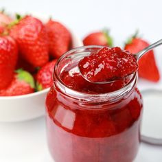 a spoon full of strawberry jam next to a bowl of strawberries on the table