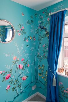 a blue room with flowers painted on the wall and a round mirror hanging above it