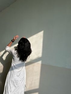 a woman standing in front of a white wall with her hands up to the ceiling