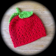 a crocheted strawberry hat sitting on top of a wooden table next to a circle