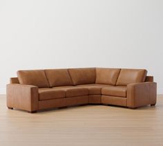 a brown leather sectional sofa sitting on top of a hard wood floor next to a white wall