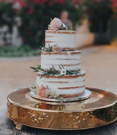 a wedding cake sitting on top of a wooden table next to a gold plate with flowers