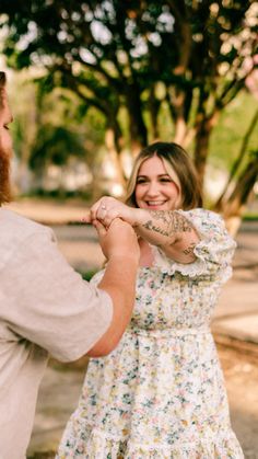 a man and woman standing next to each other in front of trees with tattoos on their arms