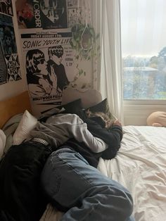 a person laying on top of a bed in front of a window next to a wall with posters