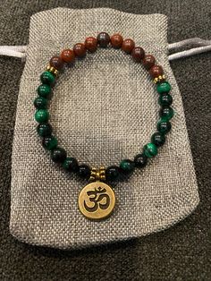 Handcrafted beaded healing bracelet with Ohm charm. Hand-strung Malachite Bracelets For Gifts, Brown Spiritual Hand-strung Stretch Bracelet, Green Malachite Spiritual Beaded Bracelets, Green Tiger Eye Bracelet, Spiritual Green Malachite Jewelry, Tiger Eye Bracelet, Healing Bracelets, Tiger Eye, Gemstone Bracelet