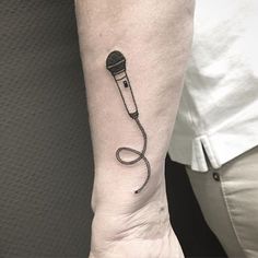 a microphone tattoo on the left inner arm is shown in black and grey ink, with a cord attached to it