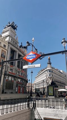 a metro sign hanging from the side of a metal pole in front of some buildings