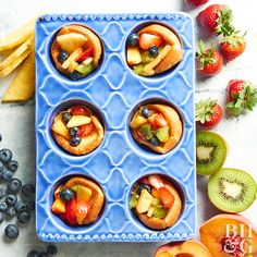 blue muffin tins filled with fruit on top of a white table next to sliced kiwis and strawberries