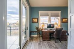 an open door leading to a home office with wood flooring and blue walls, along with two windows