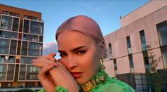 a woman with pink hair and green shirt posing for a photo in front of some buildings