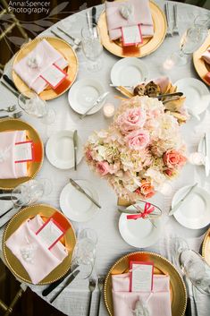 the table is set with pink napkins and white plates, silverware, and flowers