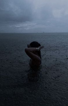 a woman standing in the water with her arms around her head looking out at the ocean