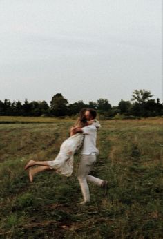 two people are playing in a field with one holding the other's back and hugging