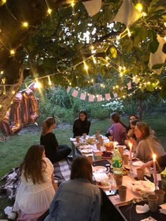 a group of people sitting around a table with food and drinks on it under a tree