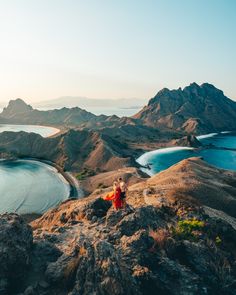 two people sitting on top of a mountain looking out at the ocean and mountains in the distance