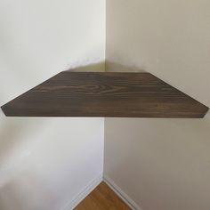 a corner shelf in the corner of a room with white walls and wood flooring