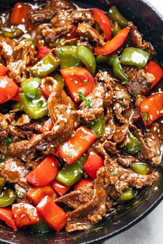 a skillet filled with meat and vegetables on top of a white countertop next to a wooden spoon