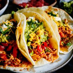 three tacos are sitting on a plate with salsa and tortillas in the background