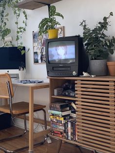 a television sitting on top of a wooden cabinet next to a table with books and plants